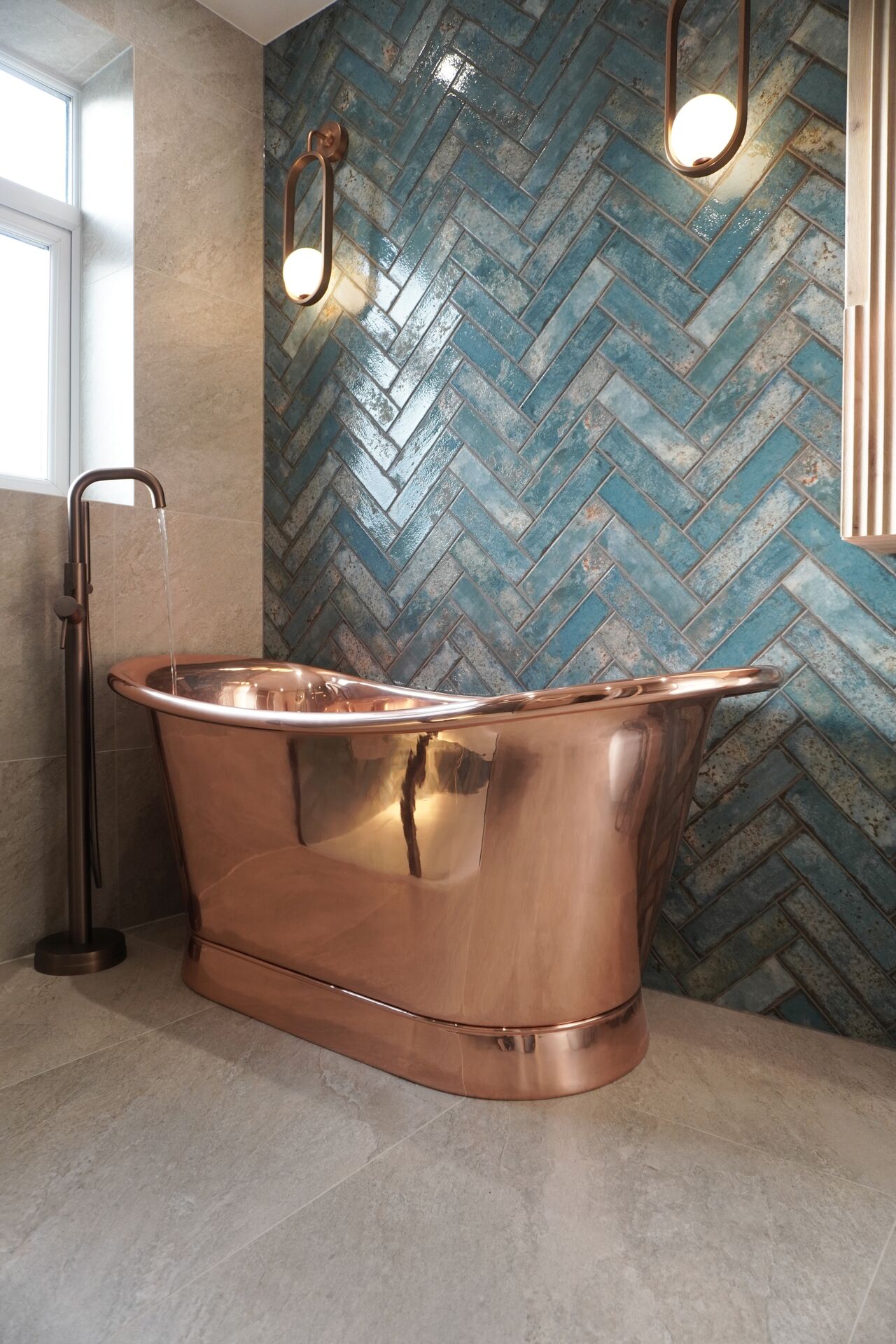 Freestanding copper bath against a blue herringbone tiled wall, part of a recent Uventi bathroom installation